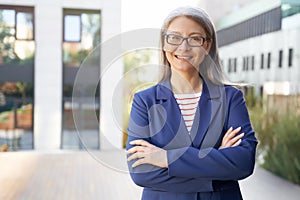 Portrait of a beautiful happy mature business woman in eyeglasses and classic wear keeping arms crossed and smiling at