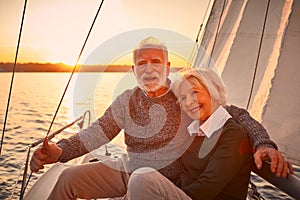 Portrait of a beautiful and happy senior couple in love hugging and enjoying amazing sunset while sitting on the side of