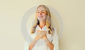 Portrait of beautiful happy smiling caucasian grateful woman put folded hands on her heart on white studio background