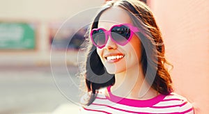 Portrait of beautiful happy smiling young brunette woman in red heart shaped sunglasses on pink background