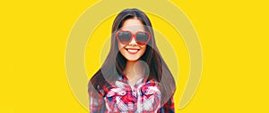 Portrait of beautiful happy smiling young brunette woman in red heart shaped sunglasses on yellow background