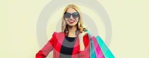 Portrait of beautiful happy smiling young woman with colorful shopping bags wearing a red business blazer on background