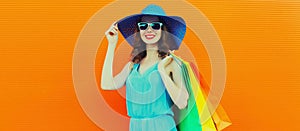 Portrait of beautiful happy smiling young woman with colorful shopping bags wearing summer straw hat on orange background