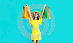 Portrait beautiful happy smiling young woman with shopping bags wearing summer straw round hat on blue background