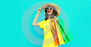 Portrait of beautiful happy smiling young woman with shopping bags wearing summer straw round hat on blue background