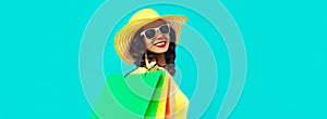 Portrait of beautiful happy smiling young woman with shopping bags wearing summer straw round hat on blue background
