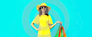 Portrait of beautiful happy smiling young woman with shopping bags wearing summer straw round hat on blue background