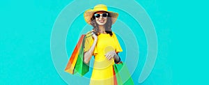 Portrait of beautiful happy smiling young woman with shopping bags wearing summer straw round hat on blue background