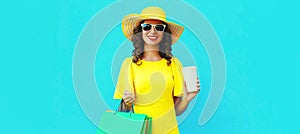 Portrait of beautiful happy smiling young woman with shopping bags wearing summer straw round hat on blue background