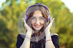 Portrait of a beautiful happy teenager girl with headphones on head, young woman listening to music on the nature