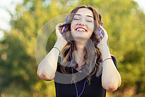 Portrait of a beautiful happy teenager girl with headphones on head, young woman listening to music on the nature in the field