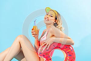 Portrait of beautiful happy woman in bathing suit sitting sexy and smiling to camera, holding rubber ring, fresh juice or cocktail