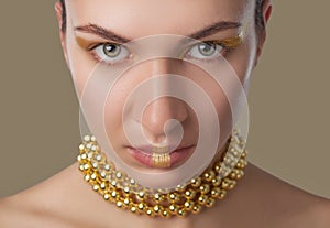 Portrait of a beautiful happy woman with beautiful creative makeup in gold colors. She has gold beads on her neck. Make-up concept