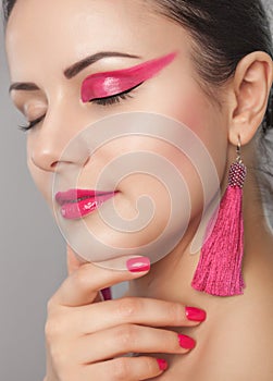 Portrait of a beautiful happy woman with beautiful creative makeup in pink colors. She has pink earrings and she has a pink