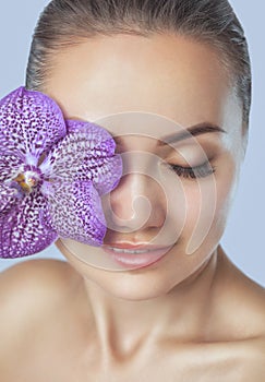 Portrait of a beautiful happy woman with clean skin and with nude make-up. She holds a beautiful purple orchid near her face.