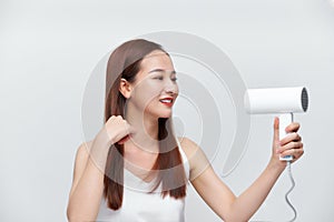 Portrait of beautiful happy woman drying her long hair with dryer over white background