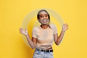 Portrait of beautiful, happy, young african girl in casual clothes posing with smile and laugh against yellow studio