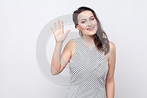 Portrait of beautiful happy young brunette woman with makeup and striped dress standing, looking at camera with toothy smile and