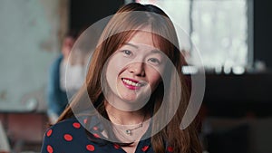 Portrait of beautiful happy young gen-z Chinese freelancer woman smiling at camera at modern busy coworking workplace.