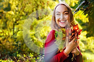 Portrait of a beautiful happy young woman with a bouquet of yellow leaves in an autumn park. A pretty Caucasian lady smiles and