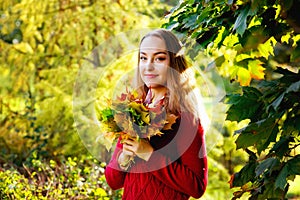 Portrait of beautiful happy young woman in casual clothes holding bouquet of yellow leaves at autumn park. Pretty Caucasian lady