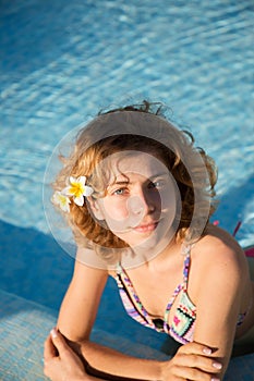 portrait of beautiful happy young woman, slender teenage girl, with curly hair, is relaxing in the water of the pool