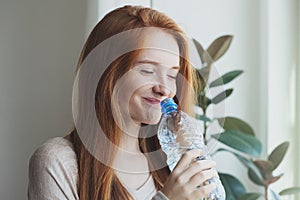 Portrait of beautiful healthy smiling red haired young woman drinking water from plastic bottle