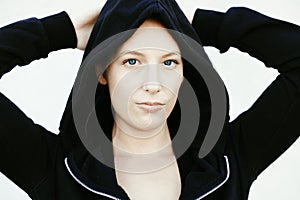 Portrait of beautiful, healthy, strong and fit young caucasian woman wearing a black hoodie flexing both arms muscles on