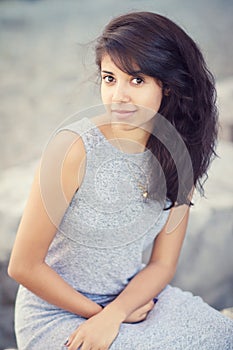 Portrait of beautiful Hispanic latino white girl woman with brown eyes, long dark curly wavy hair in gray dress sitting in park