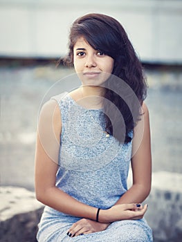 Portrait of beautiful Hispanic latino white girl woman with brown eyes, long dark curly wavy hair in gray dress sitting in park