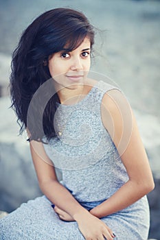 Portrait of beautiful Hispanic latino white girl woman with brown eyes, long dark curly wavy hair in gray dress sitting in park