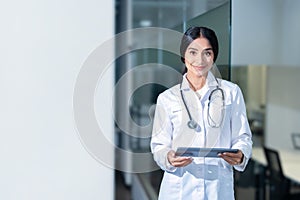 Portrait of beautiful Indian female doctor wearing white lab coat, using tablet computer