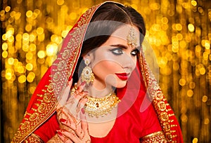 Portrait of beautiful indian girl in red bridal sari over golden bokeh. Young hindu woman model with kundan jewelry. Traditional