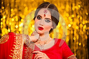 Portrait of beautiful indian girl in red bridal sari over golden bokeh. Young hindu woman model with kundan jewelry. Traditional