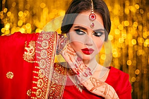 Portrait of beautiful indian girl in red bridal sari over golden bokeh. Young hindu woman model with kundan jewelry. Traditional