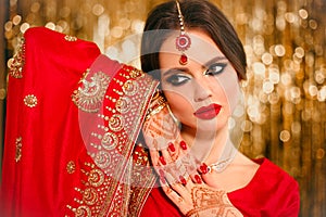 Portrait of beautiful indian girl in red bridal sari over golden bokeh. Young hindu woman model with kundan jewelry. Traditional