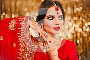 Portrait of beautiful indian girl in red bridal sari over golden bokeh. Young hindu woman model with kundan jewelry. Traditional