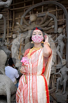 Portrait of beautiful Indian girl standing in front of Durga Idol wearing traditional Indian saree, gold jewellery, bangles and