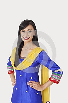 Portrait of beautiful Indian woman in traditional wear standing with hands on hips over gray background