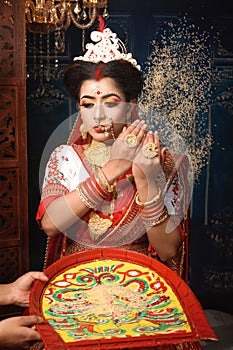 Portrait of beautiful Indian woman wearing traditional Indian saree, gold jewellery and bangles throws a handful of rice over her