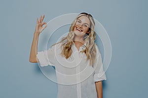 Portrait of beautiful joyful blonde girl making on camera ok gesture with fingers