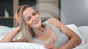 Portrait beautiful just awake woman smiling posing on bed with comfy cotton white blanket and pillow