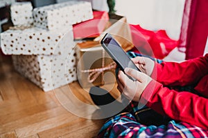 portrait of beautiful kid boy at home by the christmas tree and using mobile phone