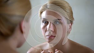 Portrait of beautiful lady looking at mirror reflection, anti-aging cream effect