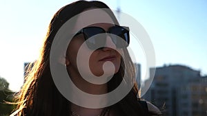 Portrait of beautiful lady in sunglasses walking at sunny day. Attractive brunette girl looks into camera going along