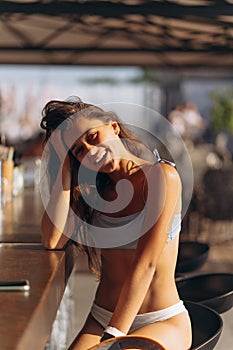 Portrait of beautiful lady in trendy swimsuit sitting at bar