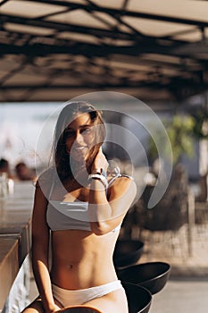 Portrait of beautiful lady in trendy swimsuit sitting at bar