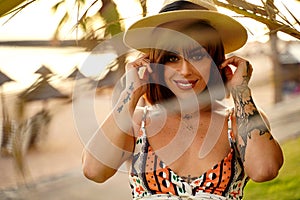 Portrait of beautiful latino woman smiling and looking at camera, wearing summer hat, posing during sunset