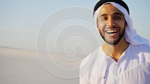 Portrait of beautiful laughing emirate male in sandy desert agai