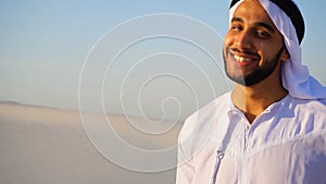 Portrait of beautiful laughing emirate male in sandy desert against blue sky outdoors